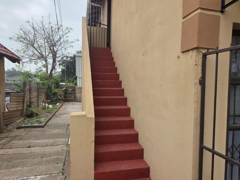 Exterior view of the property featuring an external staircase, security gate, and paved walkway leading to the rear area.