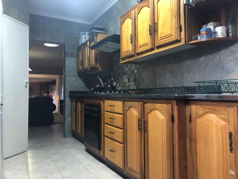 A functional kitchen featuring traditional wooden cabinetry, granite countertops, built-in oven, and gas hob with tiled wall finishes.