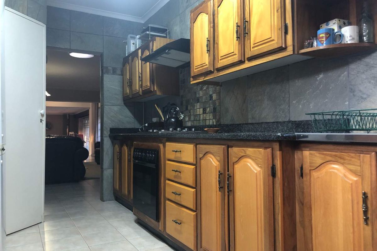 A functional kitchen featuring traditional wooden cabinetry, granite countertops, built-in oven, and gas hob with tiled wall finishes.
