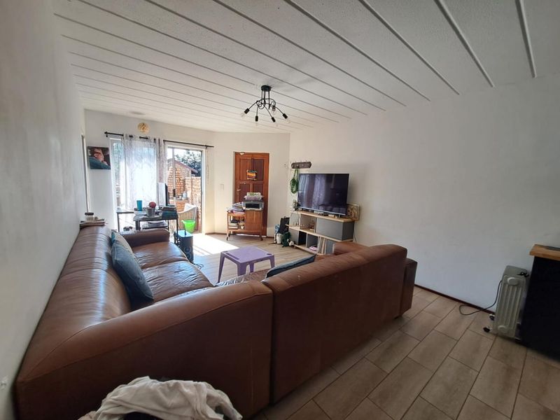 A living room featuring tiled flooring, a panelled ceiling, and a glass sliding door providing access to the exterior.
