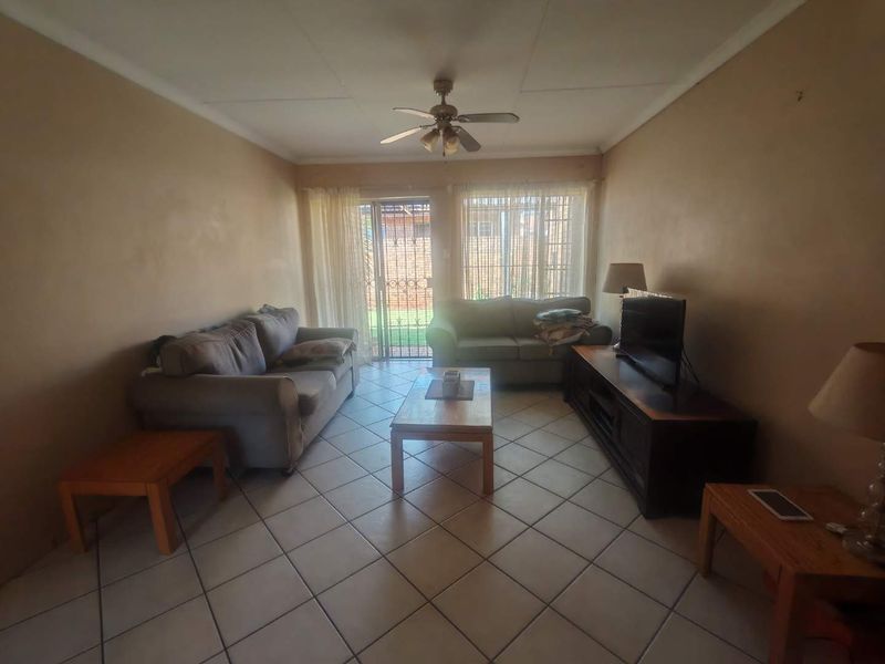 A living room featuring tiled flooring, a ceiling fan, and a sliding glass door with security gate leading to the exterior.