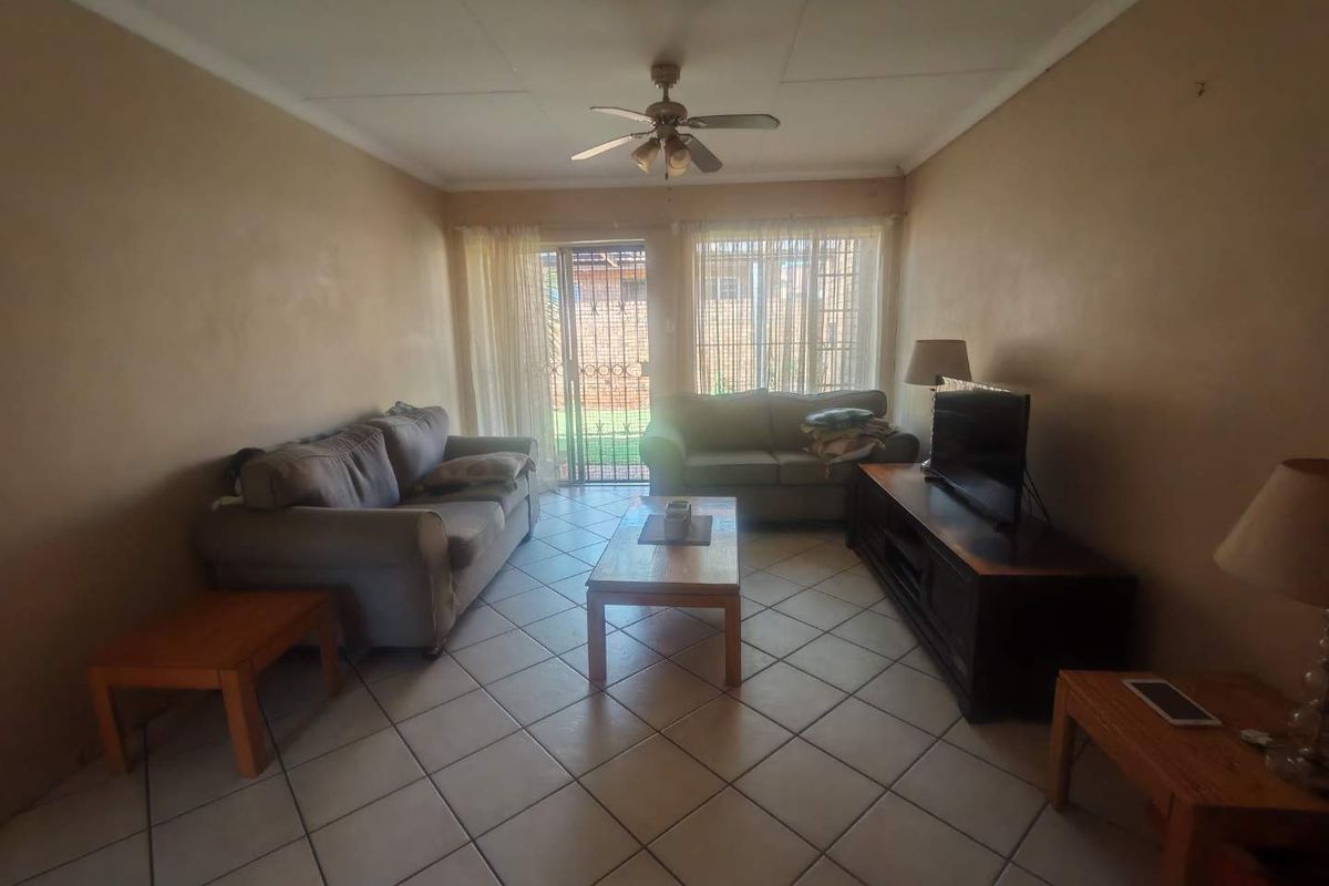 A living room featuring tiled flooring, a ceiling fan, and a sliding glass door with security gate leading to the exterior.