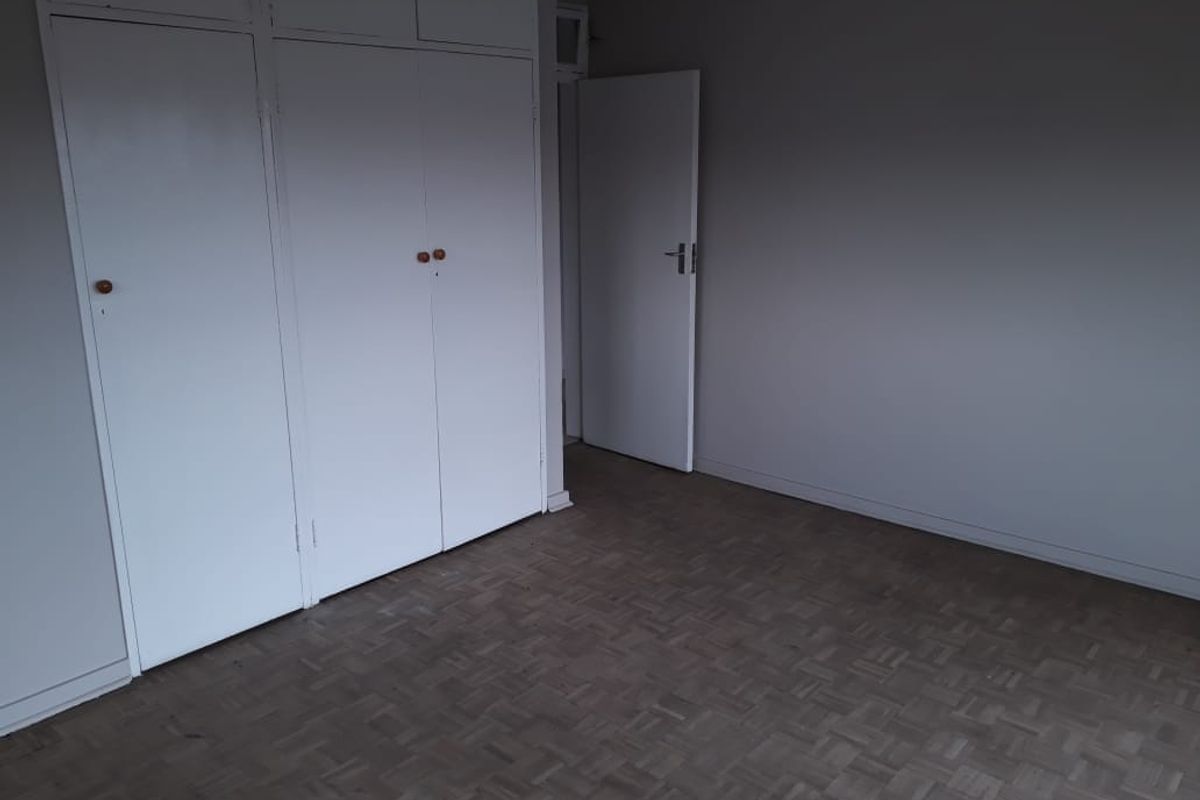 An empty bedroom featuring classic parquet flooring and ample built-in cupboard storage space.
