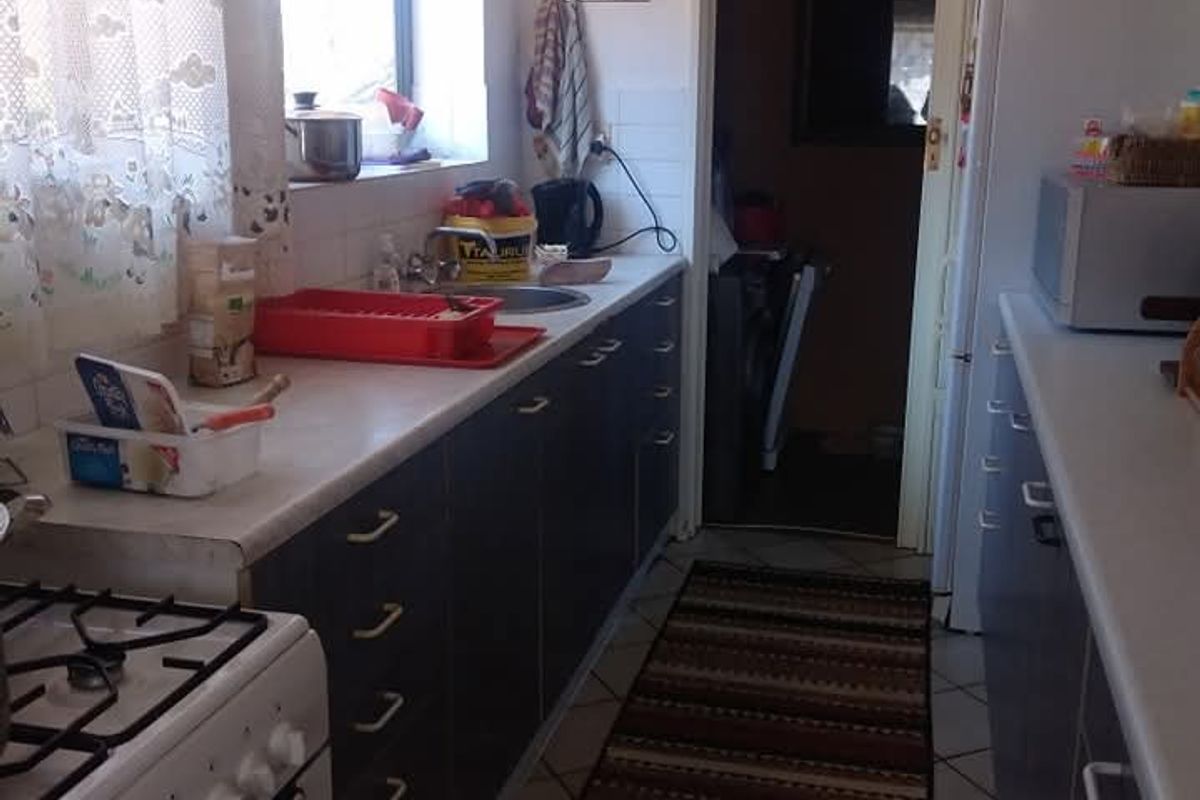 A functional galley-style kitchen featuring built-in cabinetry, a gas stove, and a stainless steel sink, with direct access to an adjacent utility area.
