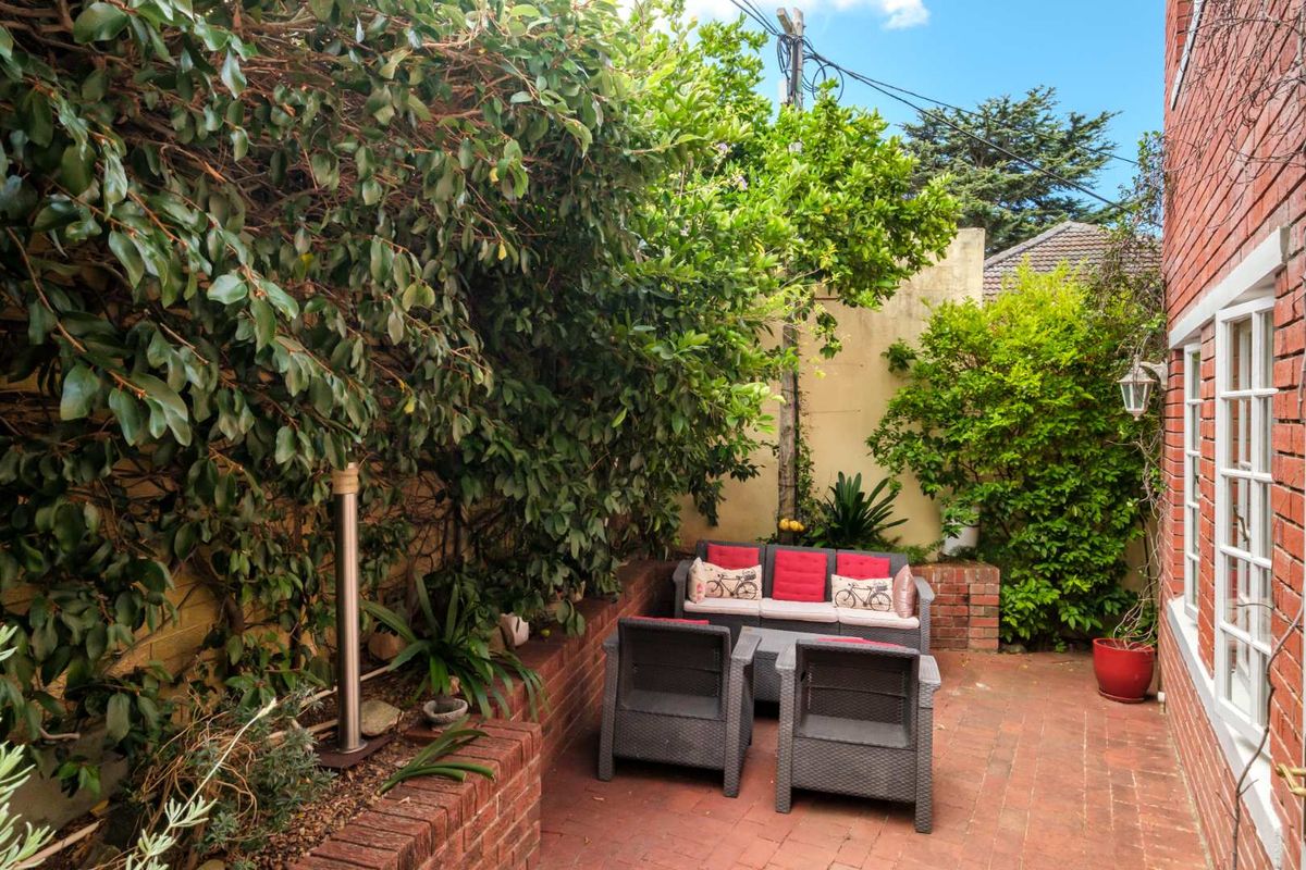 A private rear courtyard featuring red brick paving, established garden beds, and a brick retaining wall, offering a secluded outdoor living space.