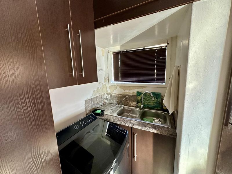 Compact scullery area featuring built-in cabinetry, a double bowl sink, and laminate countertops, currently requiring wall repairs and cosmetic refurbishment.