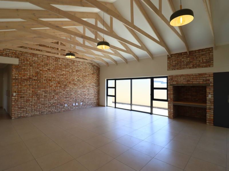 Spacious living area featuring high vaulted ceilings with exposed timber trusses, a striking brick feature wall, built-in fireplace, and large sliding doors to the exterior.