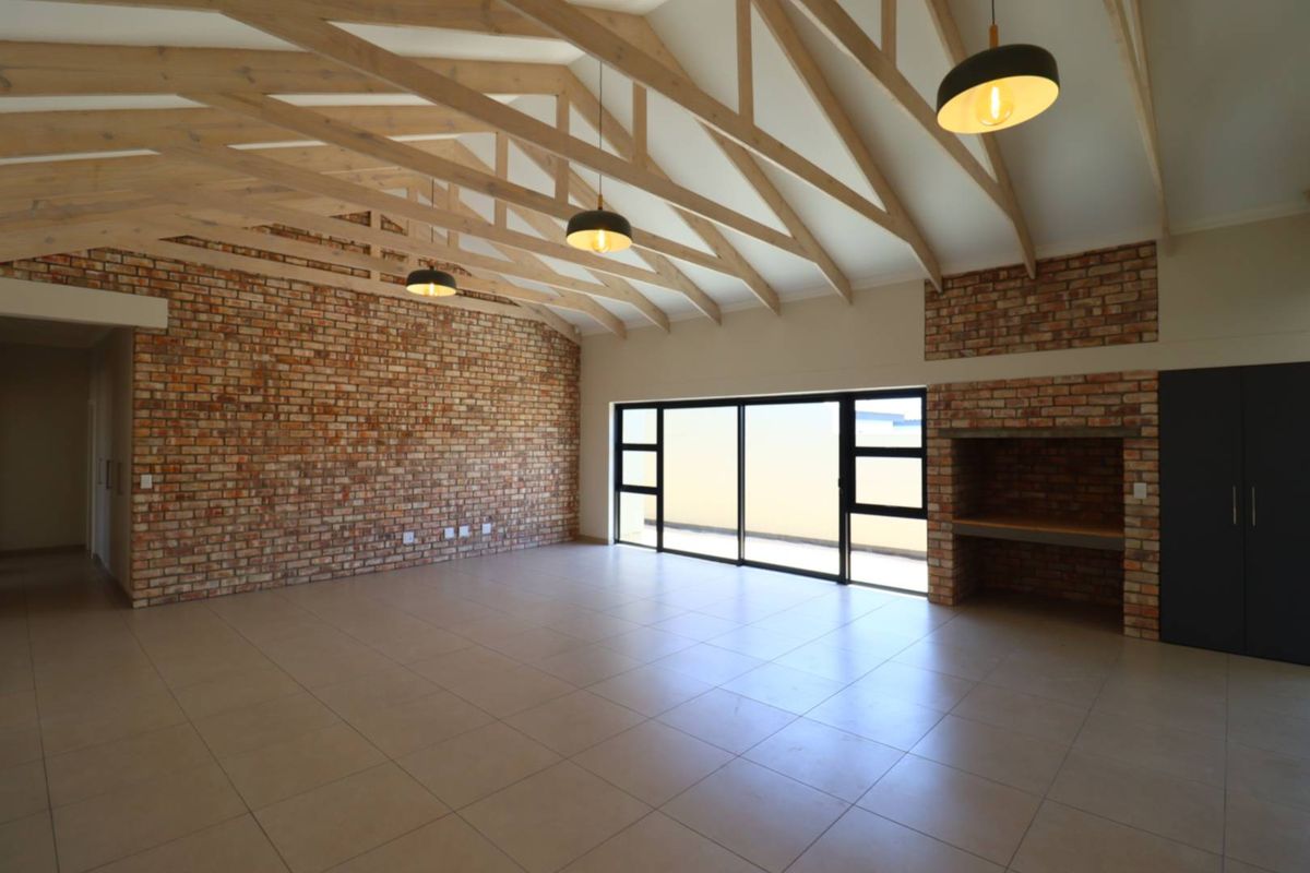 Spacious living area featuring high vaulted ceilings with exposed timber trusses, a striking brick feature wall, built-in fireplace, and large sliding doors to the exterior.