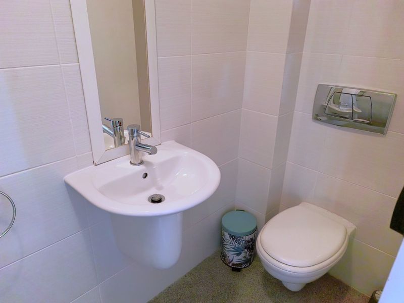 A compact, modern bathroom featuring a wall-mounted basin with chrome fixtures, a wall-hung toilet with a concealed cistern, and neutral wall tiling.