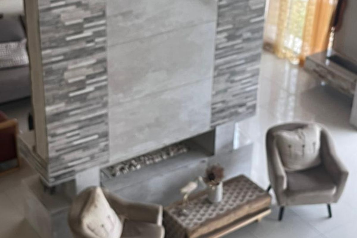 A high-angle view of a spacious living area featuring a prominent floor-to-ceiling stone-clad fireplace and large format floor tiles.