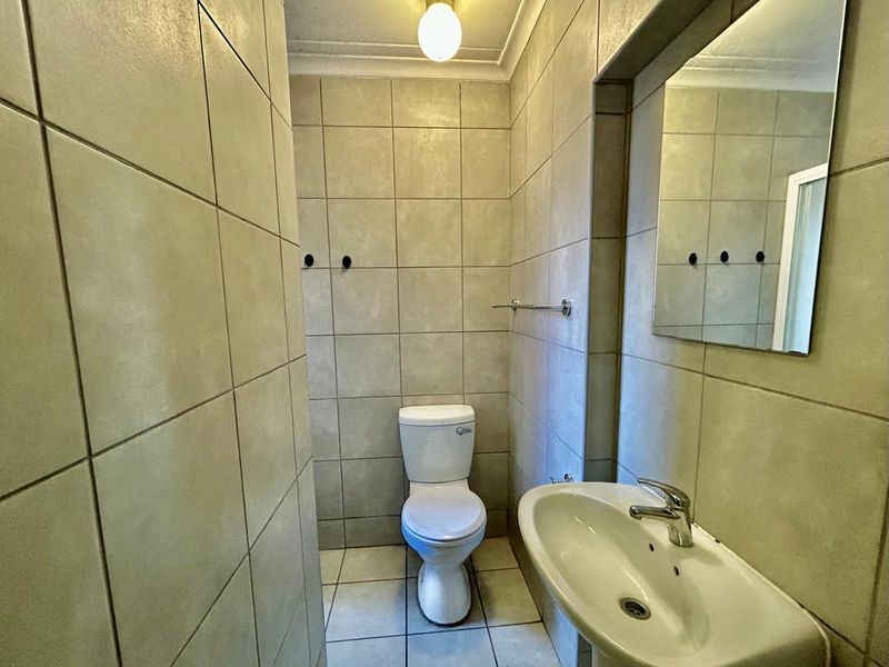 A functional bathroom featuring full-height wall tiling, a pedestal basin, a wall-mounted mirror, and a standard toilet.