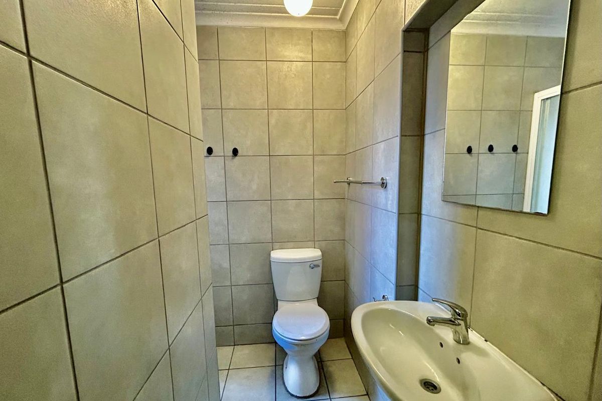 A functional bathroom featuring full-height wall tiling, a pedestal basin, a wall-mounted mirror, and a standard toilet.