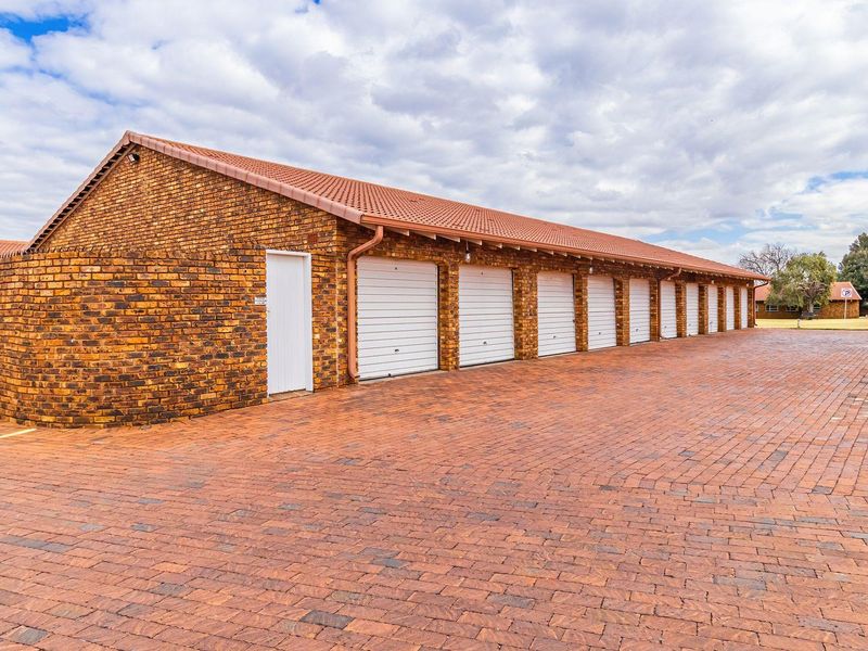 A row of secure garages with brick exterior and paved driveway access within a townhouse complex.