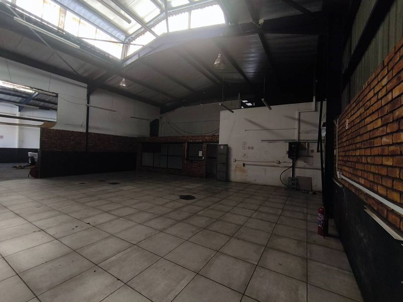 Spacious industrial utility area featuring exposed steel roof trusses, natural light from skylights, tiled flooring, and exposed brick wall accents.