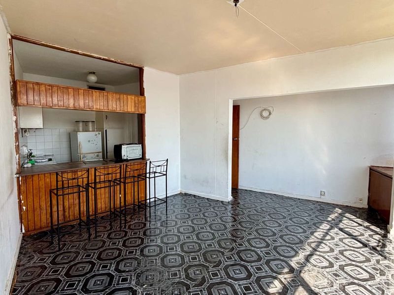 Open plan living and kitchen area featuring a breakfast bar, dated cabinetry, and patterned vinyl flooring, requiring cosmetic updates to modernize the space.