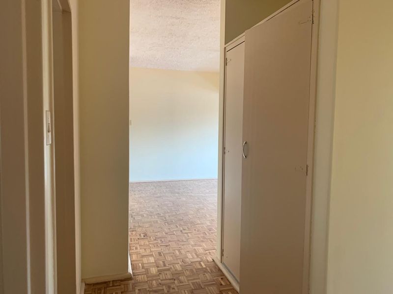 A vacant hallway featuring parquet flooring and a built-in storage cupboard, leading into an open living area.