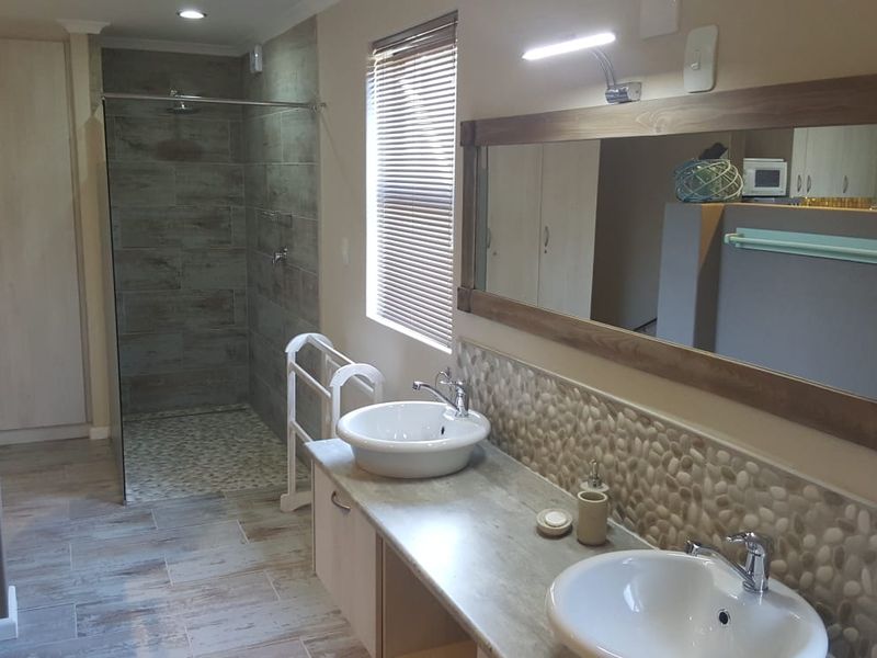 Modern bathroom featuring a double vanity with vessel sinks, pebble tile backsplash, and a spacious walk-in shower with glass enclosure.