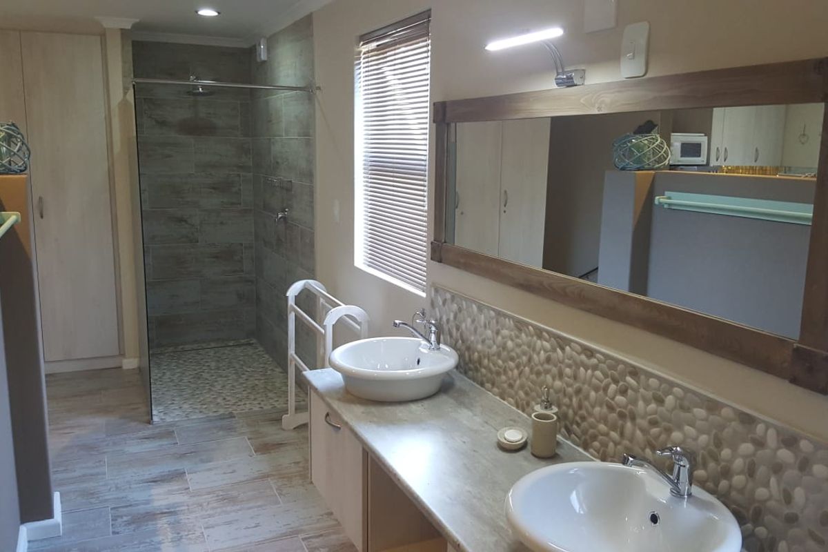 Modern bathroom featuring a double vanity with vessel sinks, pebble tile backsplash, and a spacious walk-in shower with glass enclosure.