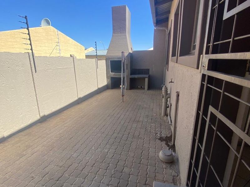 Rear exterior patio area featuring a built-in braai, paved flooring, and secure perimeter walling with electric fencing.
