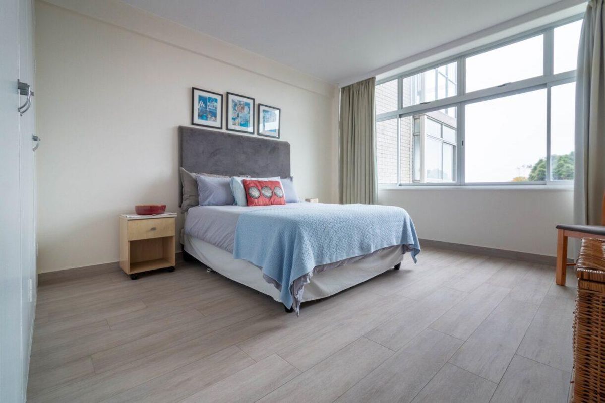 A bright and spacious bedroom featuring modern laminate flooring and a large window that allows for ample natural light.