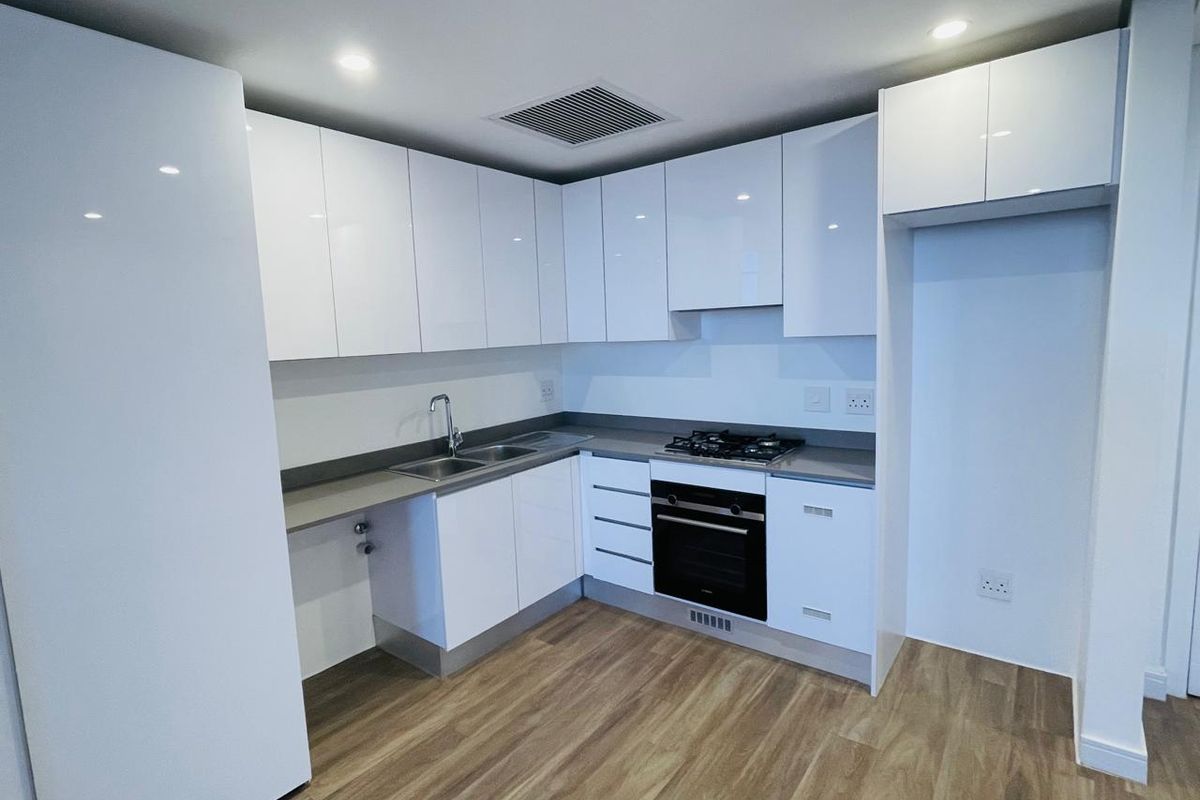 Modern kitchen featuring white high-gloss cabinetry, stone countertops, integrated gas hob, built-in oven, and wood-look flooring in a clean, contemporary apartment setting.