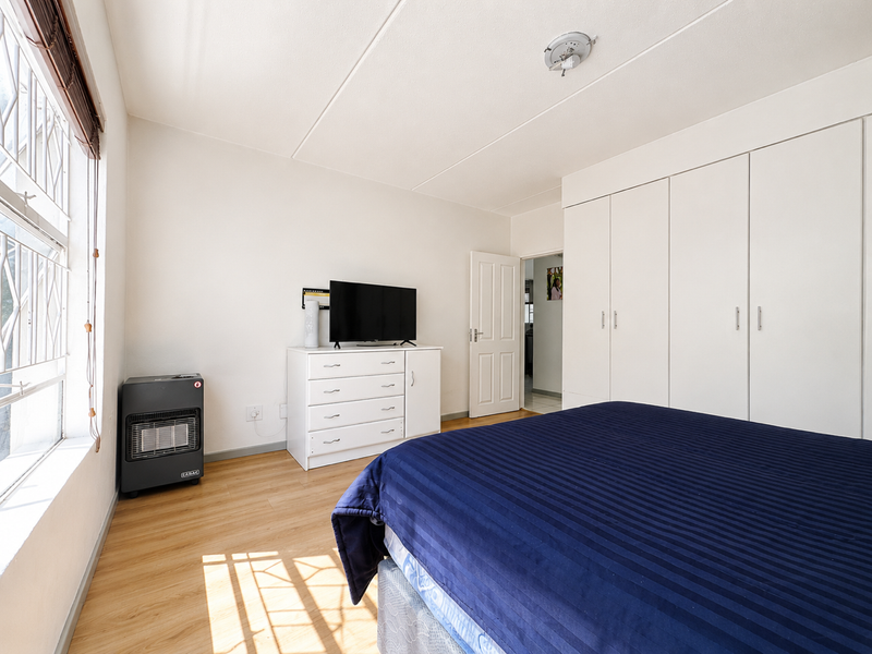 A bedroom featuring laminate flooring, built-in cupboards, and security bars on the windows, offering a functional and well-lit living space.