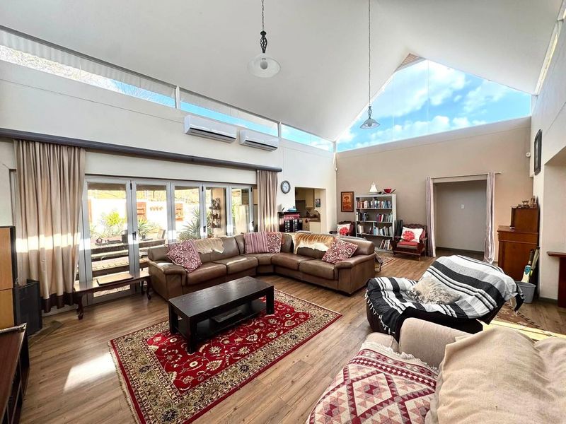 Spacious living room featuring a high vaulted ceiling, clerestory windows for natural light, dual air conditioning units, and large stacker doors opening to the patio.