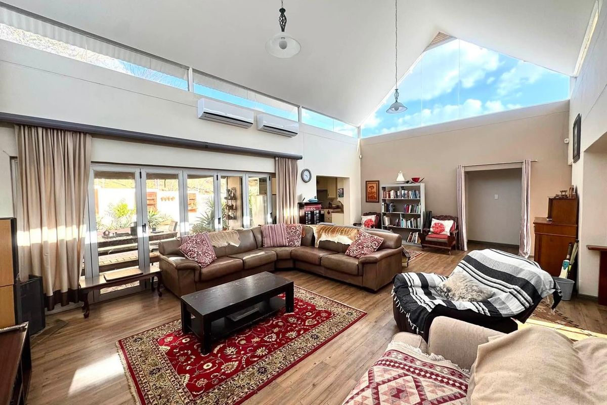 Spacious living room featuring a high vaulted ceiling, clerestory windows for natural light, dual air conditioning units, and large stacker doors opening to the patio.