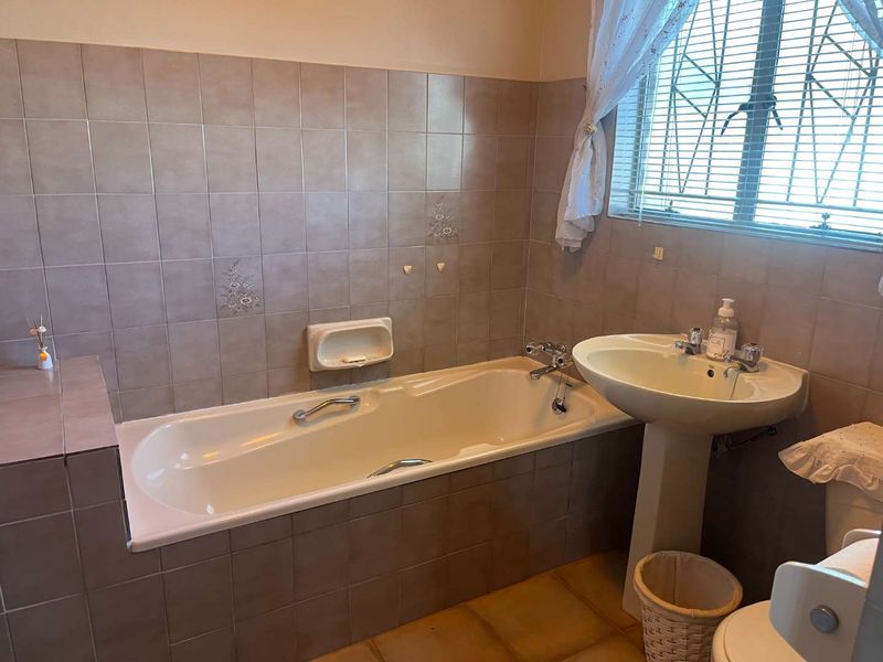 A functional bathroom featuring a built-in bathtub, pedestal washbasin, and neutral ceramic tiling throughout.