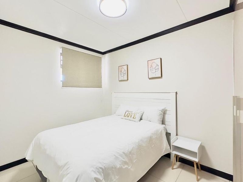 A clean and well-maintained bedroom featuring neutral tiled flooring, a roller blind, and a modern ceiling light fixture.