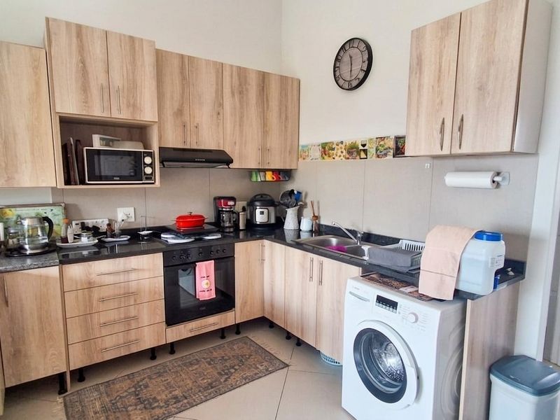 A functional kitchen featuring light wood-tone cabinetry, granite countertops, built-in oven, hob, extractor fan, and an integrated washing machine.