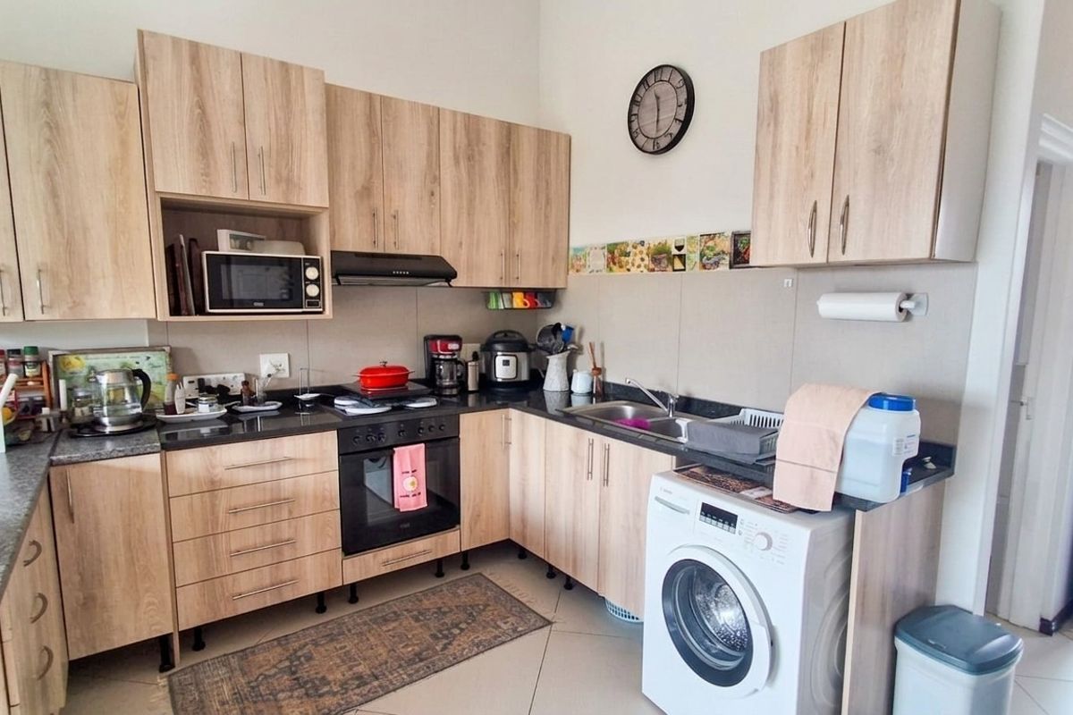 A functional kitchen featuring light wood-tone cabinetry, granite countertops, built-in oven, hob, extractor fan, and an integrated washing machine.