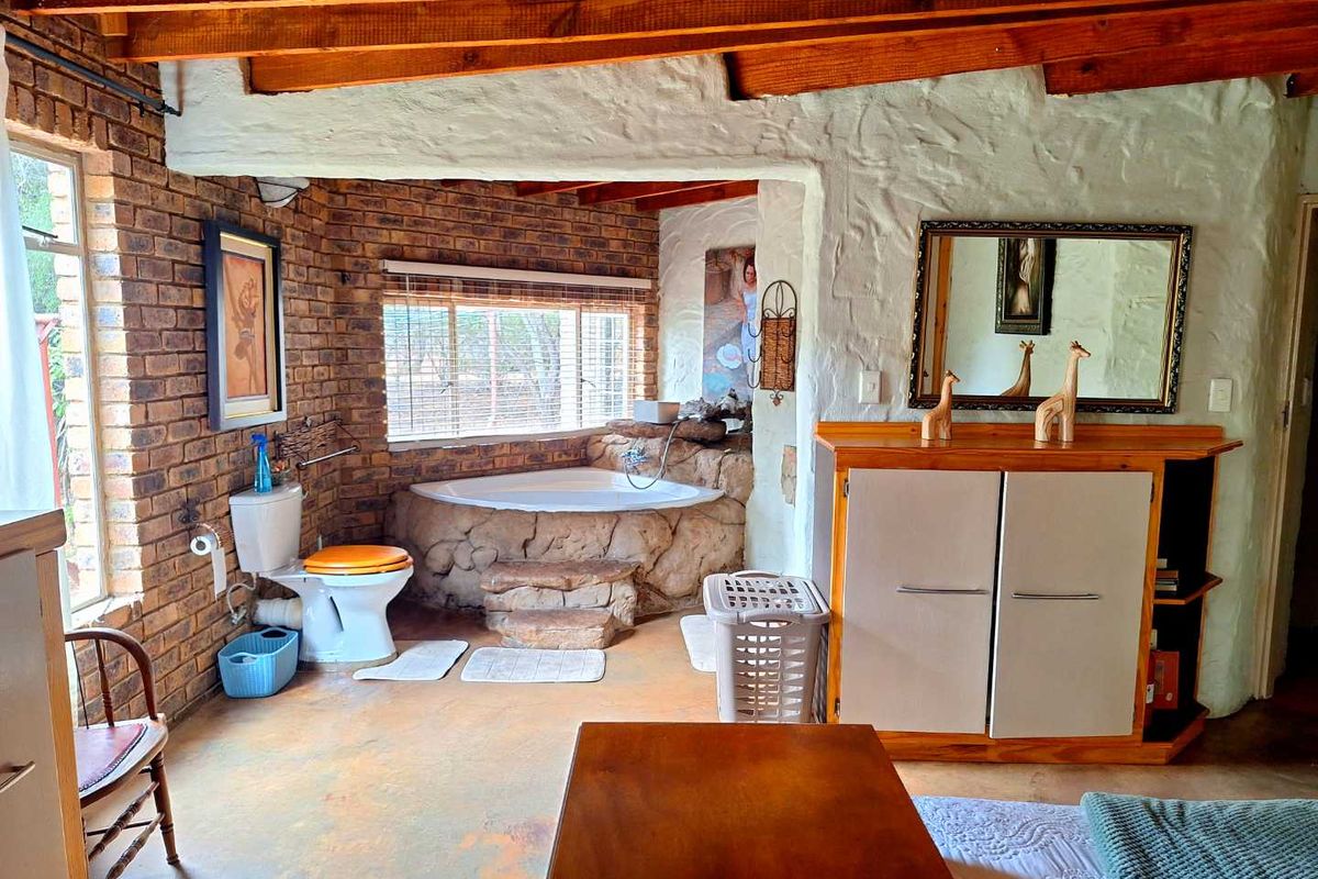 A rustic-style bathroom featuring exposed brick walls, a built-in stone-clad bathtub, and exposed timber ceiling beams.