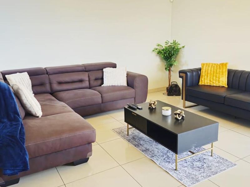 A spacious living room featuring neutral tiled flooring, cove cornicing, and a central ceiling light fixture, providing a clean and functional living space.