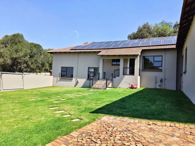 Rear view of the house featuring a well-maintained lawn, stone pathway, and a roof equipped with solar panels.