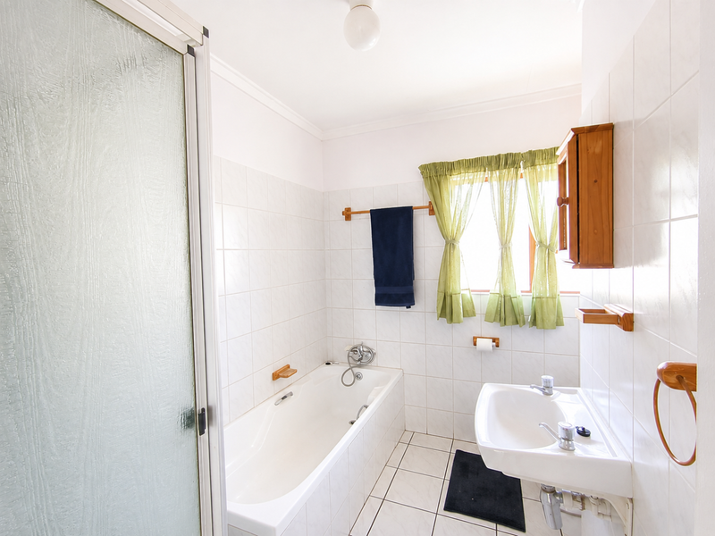 A functional bathroom featuring a bathtub, separate shower enclosure, and wall-mounted basin with white ceramic tiling throughout.