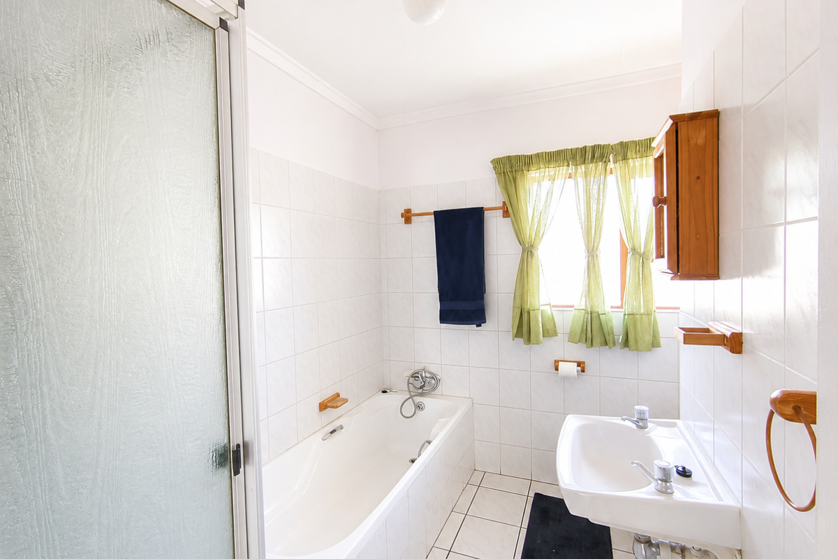 A functional bathroom featuring a bathtub, separate shower enclosure, and wall-mounted basin with white ceramic tiling throughout.