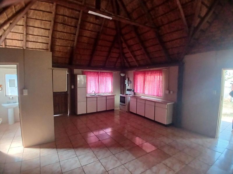Open-plan kitchen and living area featuring a high thatched roof with exposed timber beams and tiled flooring, offering a rustic cottage aesthetic.