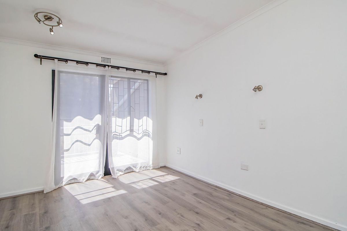 A bright, empty bedroom featuring light-toned laminate flooring, neutral walls, and a sliding glass door with access to an outdoor area.
