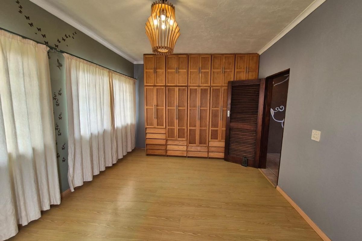 Spacious bedroom featuring extensive built-in wooden cabinetry, laminate flooring, and neutral wall tones, offering a clean and functional living space.