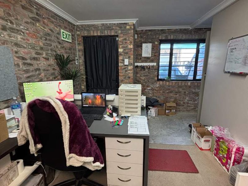 A functional office space featuring exposed brick walls, fluorescent lighting, and a window, currently utilized as a workspace.