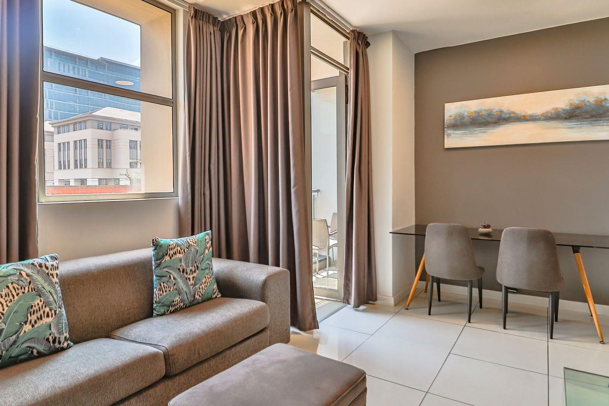 A bright living room featuring large windows, tiled flooring, and direct access to a private balcony, creating a comfortable and well-lit living space.