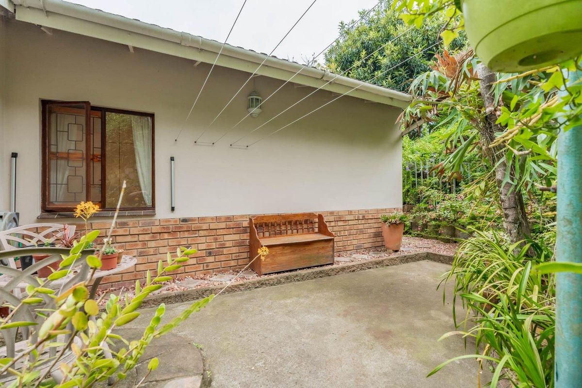 A private rear patio area featuring a concrete floor, brick base wall, and wall-mounted washing line, set against a landscaped garden backdrop.