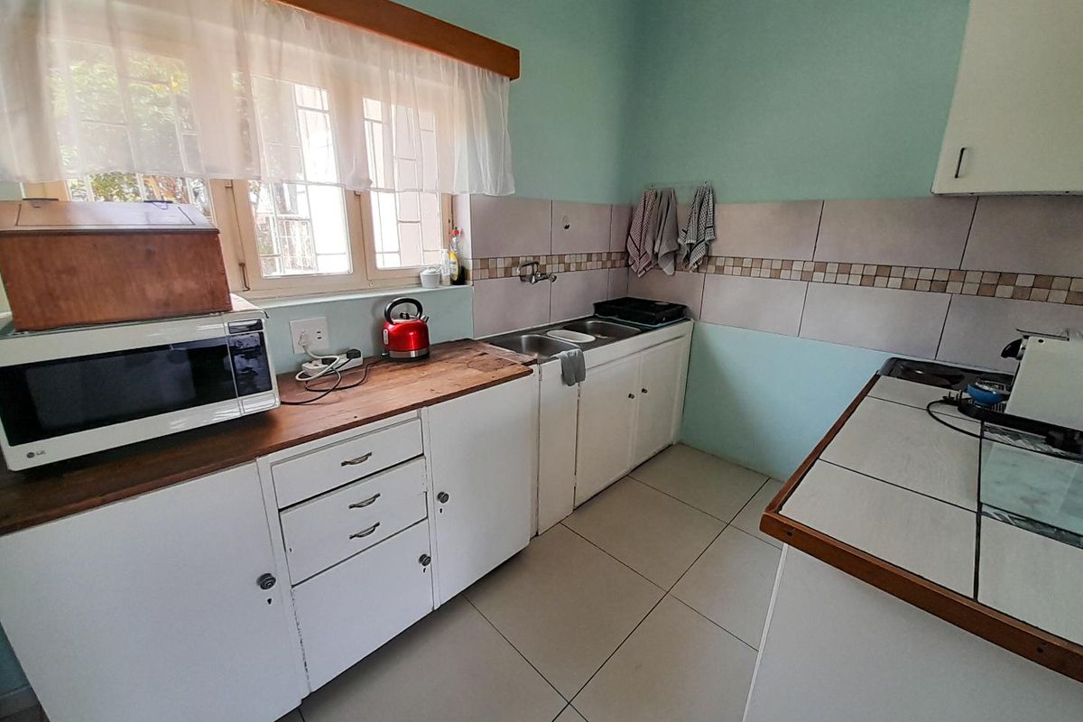 A functional kitchen featuring white cabinetry, tiled splashbacks, a double sink, and tiled flooring, offering a practical layout for daily meal preparation.