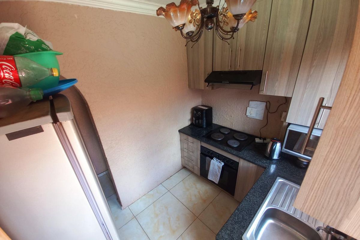 Compact kitchen featuring built-in cabinetry, integrated electric hob, oven, extractor fan, and a stainless steel sink with granite-look countertops.