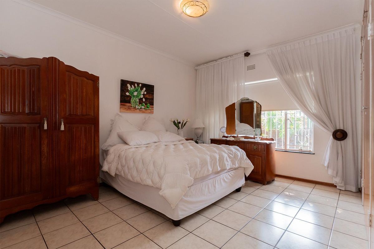 A well-lit bedroom featuring tiled flooring, built-in cupboards, and a window with security bars, offering a functional and comfortable living space.