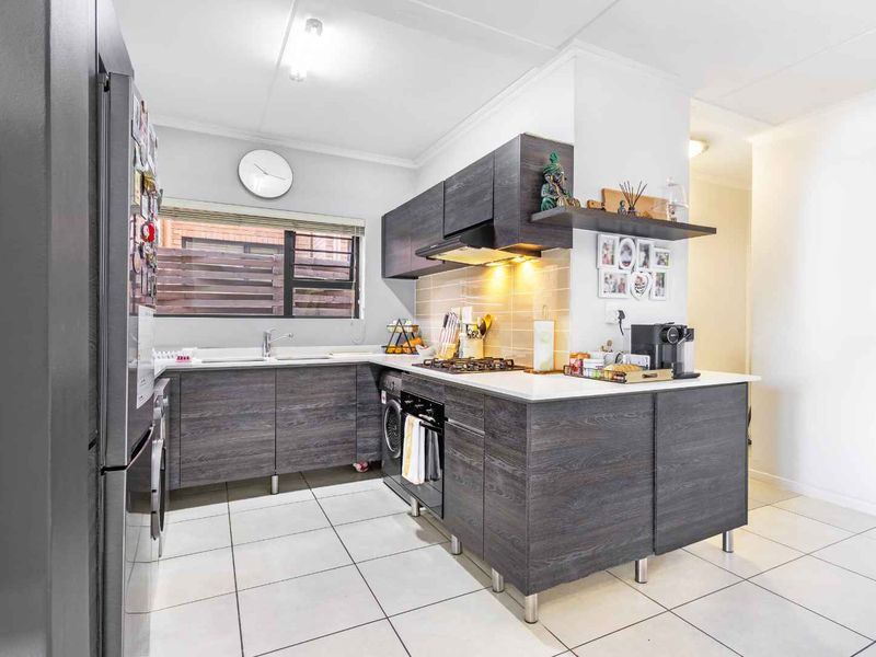 Modern kitchen featuring dark wood-grain cabinetry, stone countertops, a gas hob, built-in oven, and tiled flooring with a functional layout.
