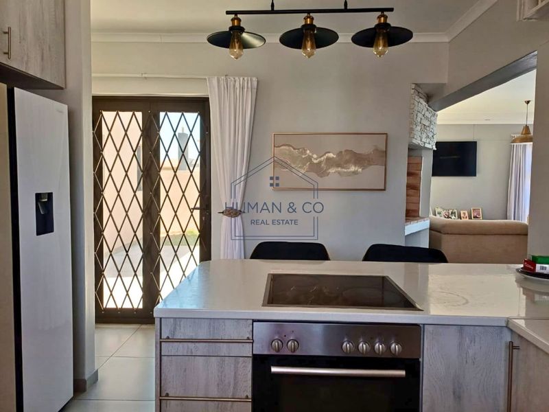 Modern open-plan kitchen featuring a central island with built-in oven and hob, flowing into the living area with access to an outdoor patio.