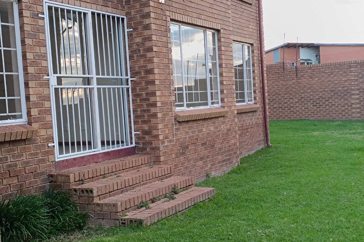 Rear view of the townhouse featuring face-brick exterior, security gates, and a private grassed garden area.