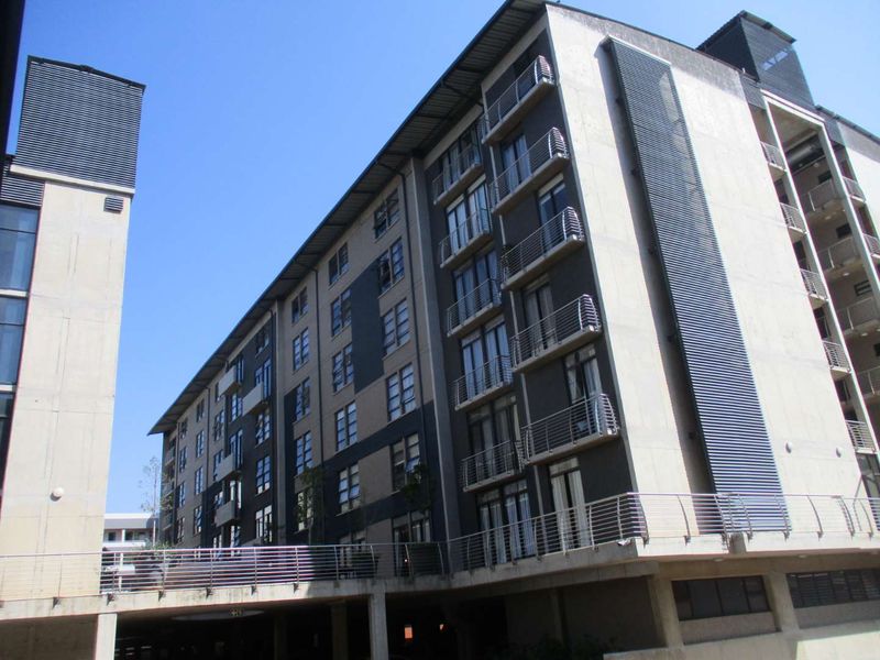 Modern multi-story apartment building featuring concrete facade, private balconies with metal railings, and ground-level undercover parking.